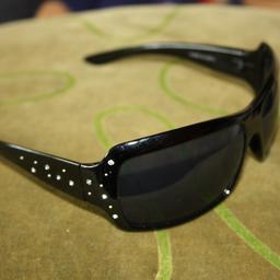 Schwarze Sonnenbrille aus Kunststoff von Dandash. Glitzersteine auf den Bügeln.

UV 400, Kategorie 3