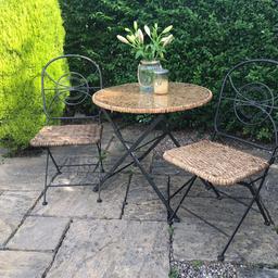 A lovely bistro table and 2 chairs set made with steel frames with rattan seat base and table top that neatly fold away. 

The table has a circular glass panel that sits on the top to create a flat surface for your drinks glasses and wine bottle. 

Perfect for enjoying the sun in these autumn months 

Some cosmetic fraying to the wicker seat but doesn’t affect the integrity of the chairs. Could be painted 

Collection from Birstall WF17 or delivery within 40 miles for an additional fee