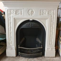 Elegant victorian style cast iron fireplace with attachable wooden shelf, measures approx 106cm wide, 105cm high. Flue vent needs adaptation for open fire - currently sealed with plasterboard. There are a few cracks in the metal surround, sealed at the back (with a cement-like substance), and other signs of wear / use - on the fire insert, and a small groove on the wooden shelf.