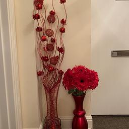 A tall metal red floral light and a tall red vase with artificial red flowers.