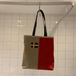 Väska i beiget och rött med en inplastad svensk flagga. Likadan på båda sidor. 

Väskan är 35 cm hög. Nyskick, använd någon enstaka gång. Passar perfekt att använda istället för matkasse så kan man bära i handen eller på axeln. Fungerar förstås även som handväska. 

Titta gärna på mina övriga annonser också. Kan skickas mot porto.