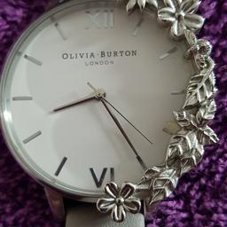 Olivia Burton Watch as seen in pics. Pale Grey strap, white face, silver hands, attached silver flower design... Extremely great condition as hardly worn.. Comes fully gift boxed..  Collect from Lowestoft NR32 4HG Or can deliver locally or post available...