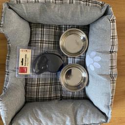 Small dog bed, padded all over in polyester. Colour is grey. Black and white check pattern. Weight up to 8-10kgs. Two small dog bowls in stainless steel grey and blue with black paw prints. Black retractable and extendable with brake button for dog weights up to 20kgs. The bed and bowls were used only once. Lead is still in the packet. Bowls and bed has been washed. Very good condition.