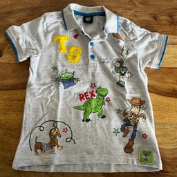 Jungen Toy Story Shirt. Dieses Polo-Shirt kommt mit stylischen blauen Streifen am Kragen und an den Ärmeln, mit einem klassischen Viertelknopfverschluss. Dieses Disney Shirt zeigt aufgestickte Designs von den Favoriten aus Andy’s Spielzeugkiste: Sheriff Woody, Rex, Alien und Buzz Lightyear.