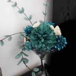champagne style vase with teal coloured flower arrangement with glass pepples