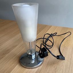 A simple fixed glass and silver base uplighter table lamp from BHS. The silver base has a silver stem through it leading to the bulb holder which fits screw in light bulbs. The lamp takes a max 60w bulb. The fixed thick glass shade starts clear at the bottom third and is then frosted for the remaining two thirds. The lamp switches on and off via a black switch on the lead. The lamp is in good condition, perfect working order the lamp comes from a smoke free home.
