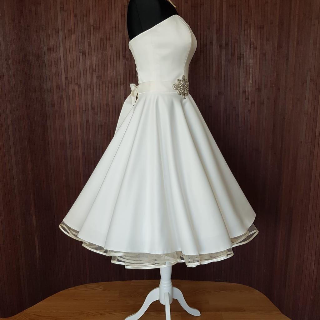 Dieses wunderschöne Petticoat Brautkleid in Ivory ist eine moderne Kombination aus schlichten, eleganten Stoffen und zeitloser Eleganz.

Das knielange Kleid mit einem weitausgestellten Swing Rock sorgt für eine traumhafte Figur und ist absolut edel.

Unglaublich sexy wirkt das Dekolleté mit Herzform-Ausschnitt. Der geschnürte Rücken, sowie der Strass-Bindegürtel ergänzen den magischen Braut-Look stimmig. Dieses wunderschöne Kleid kann mit und ohne Petticoat wunderbar getragen werden. Beides sieht traumhaft schön aus.

Hier haben wir einen 2-lagigen Petticoat mit Satinvolant in Ivory gewählt. Diesen finden Sie in unseren Anzeigen.

Das Kleid wird ohne Petticoat verkauft. Dieser kann bei Bedarf extra erworben werden.