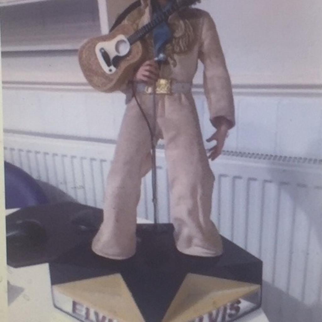 This is EXTREMELY RARE and ALMOST IMPOSSIBLE TO FIND IN THE UK as was never released here

The Doll itself is just over 50cms and stands on a base unit with speaker.

In the side compartment there is a tiny cassette tape (see pics) and when that this placed into the side of the base unit Elvis sings Hound dog and the stage flashes different colours (see pics). There is no volume control and plays song quietly.

Also the Guitar has a button that when pressed Elvis sings Blue Christmas and lights up (see pics).

Released in the very early 80s this over 40 years old so as you would expect there is some wear and some marks on the costume, however for its age it is in EXCELLENT CONDITION.