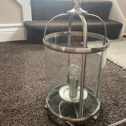 Silver metal lantern lamp.
The glass panels do remove easily.
There is a small chip to one panel at the bottom but doesn’t effect the lamp in anyway (see photo 2).
Takes a small screw bulb and has a switch to turn on and off.
Makes a great table lamp.
