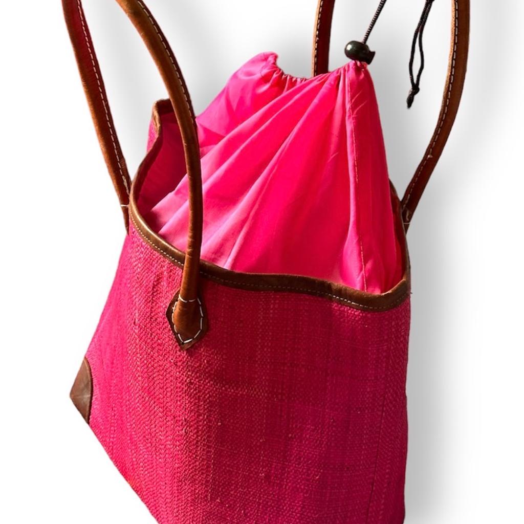 Raffia Magenta Medium Tote Bag with Leather Handles
Looking for a unique and gorgeous everyday tote? This vibrantly colorful and practical luxurious Tote bag has been handwoven from high-quality 100% raffia palm and dyed a vibrant magenta with eco-friendly dyes.
Besides being crafted in super lightweight material, this durable bag features a Tote style, a breezy woven style, reinforced vegan leather corner protectors for an extra chic touch, vegan brown leather handles just long enough to go over the shoulder, open top with a coordinating polyester cloth drawstring top closure, a raffia inner pocket sewn in, and a modern, structured shape.
A fun and fabulous bag to be your ideal companion for work or play due to its generous compartment. Easily accommodates laptops and work documents etc or useful for shopping in the city center or can perfectly fit a beach towel and other sunny day essentials.
It's the go-to tote bag of the summer!
This bag is handmade which makes it chic and un