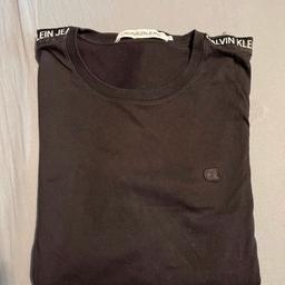 Zum Verkauf steht ein schwarzes Calvin Klein Tshirt in Größe M. Unten am Saum ist ein kleines Loch, wie auf dem Foto zusehen ist.
