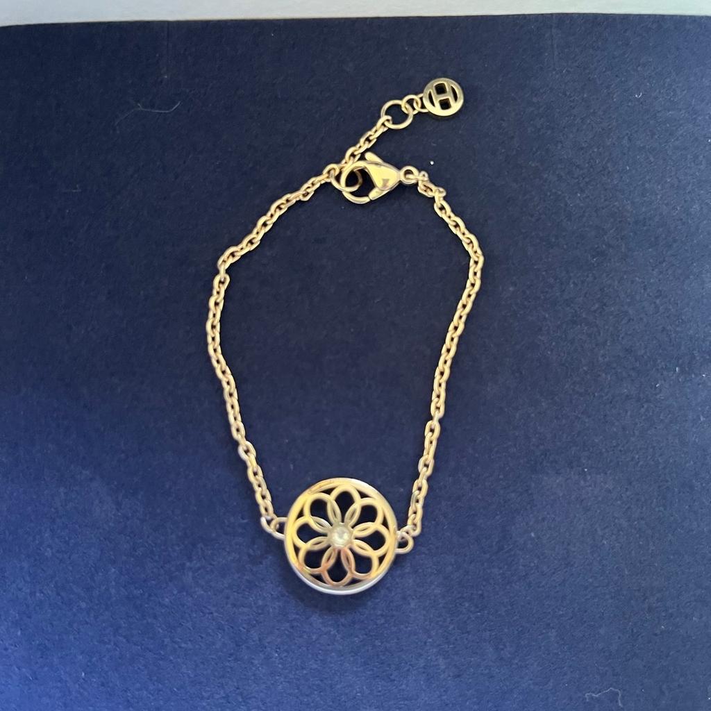 Goldenes Armband von Tommy Hilfiger mit einem großen Ornament in der Mitte, mittig ist noch ein kleiner Stein drin. Das Armband ist längenverstellbar und wird in der Original Schachtel verkauft. Kaum getragen, daher wie neu.