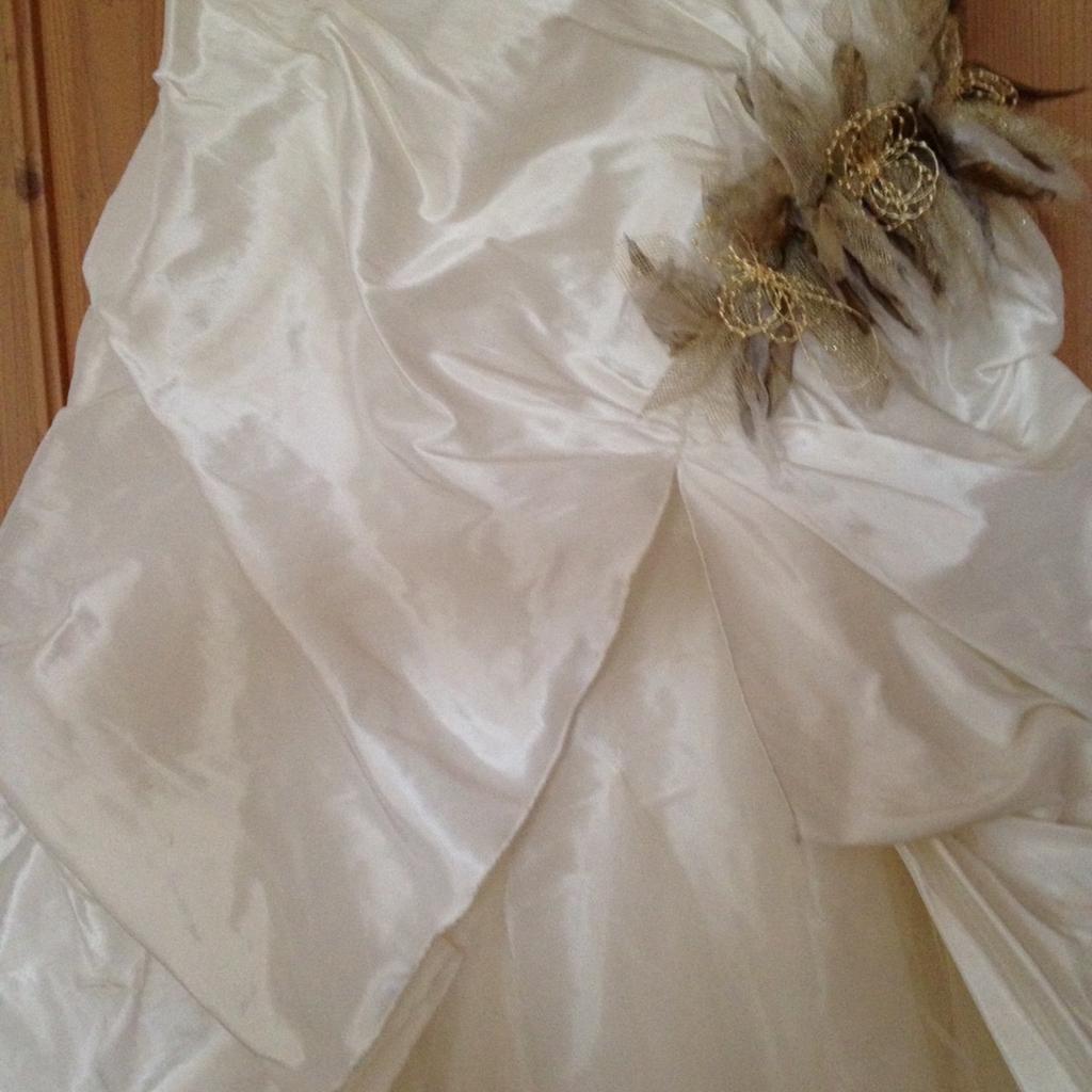 Möchte mit meinem wunderschönen Brautkleid (plus Stola/Schal) von Linea Raffaeli (gekauft bei Hänsel & Gretel) einer anderen Braut ein Schnäppchen und viel Freude bereiten!
Das Kleid hat die Gr. 36 und wurde auf meine Körpergröße von 164 cm plus
6 cm hohe Schuhe gekürzt. Besonders schön ist die kurze, spitz zulaufende Schleppe, die durch Druckknöpfe an der Innenseite hochgesteckt werden kann.
Die Farbe des Kleides wird als ivory (nicht ganz weiß) bezeichnet und der gecrashte Taftstoff hat einen wunderschönen Glanz. Das in kleine Falten gelegte Oberteil (mit Reißverschluss am Rücken) geht in einen drapierten Rock über, der an der linken Seite durch "Tüllblumen" hochgehalten wird.
Dieses Blumenmotiv in Gold- und Brauntönen findet sich auch auf der goldfärbigen Stola wieder.
Ich habe die Stola in der Kirche über die Schultern und danach als Schal, mit den Blumen an der Seite, getragen.
Das Kleid plus Stola wurde natürlich nur ein Mal getragen und danach sofort professionell gereinigt. Es