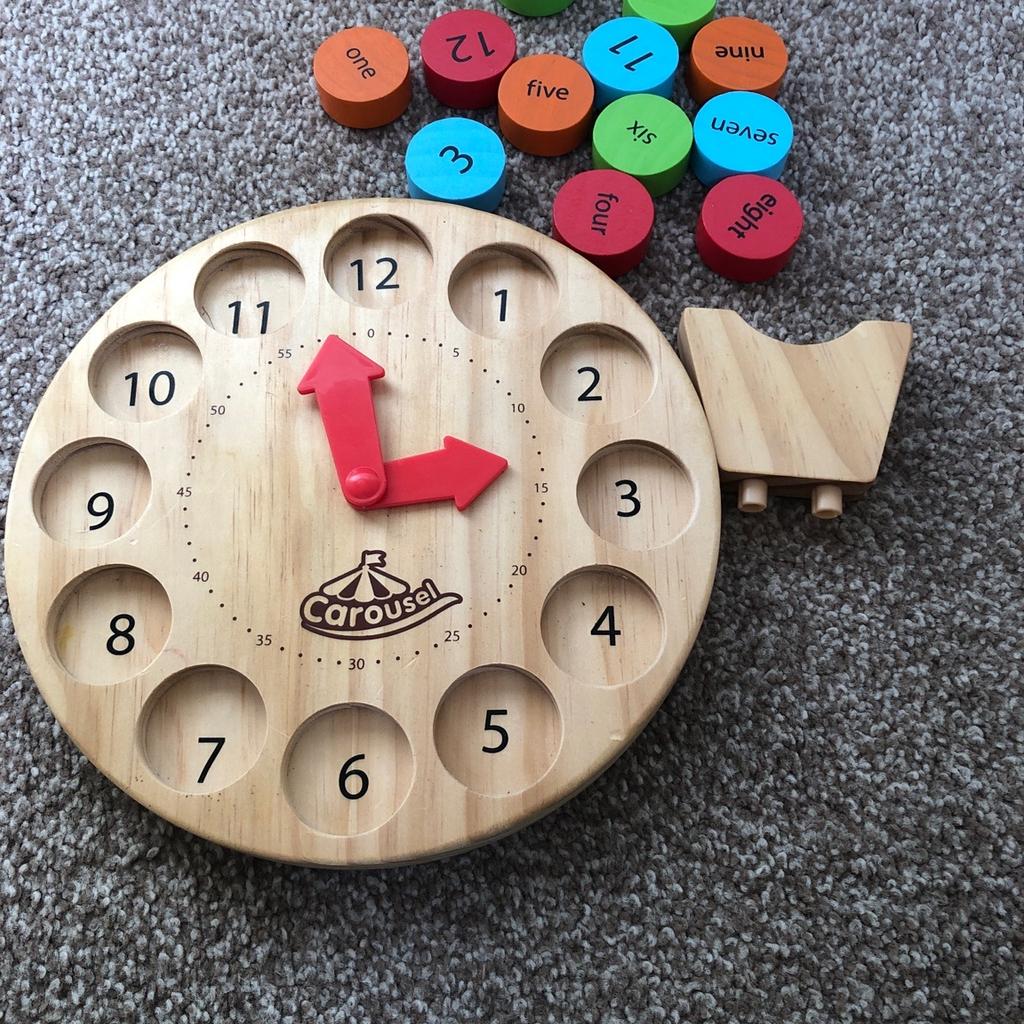 Wooden toy clock. You can take numbers out and put them back in the slots. Numbers have two sides one with the written word and the other with the number. Clock hands move and stand is removable from back.