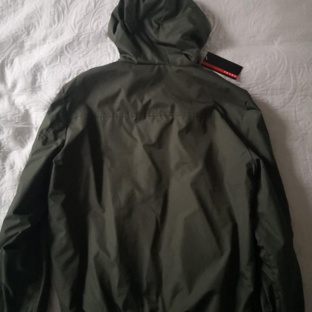 Prada Hooded Bomber Style Outdoor Rain Jacket. Brand new with tag. Size XXL, but would also fits XL. 2 Zipped side pockets, 1 zipped breast pocket, 1 zipped arm pocket and pouch. Lightweight, not padded or quilted. Selling due to car purchase, cash needed! Excellent quality and value compared to original price! Collection preferred, as too valuable for posting and buyer must try on for size and satisfaction. However, I'm prepared to post via insured, tracked and signed for postage at extra cost of £20. Must sell, hence asking such a low bargain price of £195, which is significantly lower than the true value of this item!