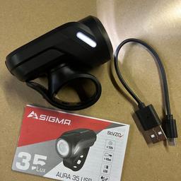 Neu, wurde nicht benutzt

SIGMA AURA 35 USB Scheinwerfer
Die AURA 35 USB von SIGMA SPORT ist der zuverlässige Begleiter für alle, die ein günstiges und wiederaufladbares Fahrradlicht in der Stadt suchen. Die 35 Lux starke Fahrradbeleuchtung ist leicht am Lenker zu befestigen und verfügt über eine uneingeschränkte StVZO Zulassung. Seitliche Leuchtelemente verbessern die Sichtbarkeit für andere Verkehrsteilnehmer. Die Fahrradlampe überzeugt mit sportlich kompaktem Design und 45 Metern Leuchtweite.

Features - AURA 35 USB

Zwei Leuchtmodi: Durch einfaches Drücken der Taste wechselt die AURA 35 USB zwischen den Leuchtmodi Standard und Eco. Der Nutzer hat die Wahl zwischen 35 Lux bei durchschnittlich 5 Stunden Leuchtdauer oder reduzierten 15 Lux bei 12 Stunden Leuchtdauer.
Wiederaufladbar: Die AURA 35 USB besitzt einen integrierten Akku. Dieser wird über die Micro-USB Buchse nachgeladen, was auch an jedem PC möglich ist