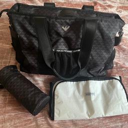 A smart black changing bag by Emporio Armani, made from smooth, silky nylon. It has a large adjustable shoulder strap, exterior pockets and adjustable, fixed stroller straps. The bag has a roomy main compartment with internal pockets and comes with a handy, changing mat and an insulated bottle bag.
