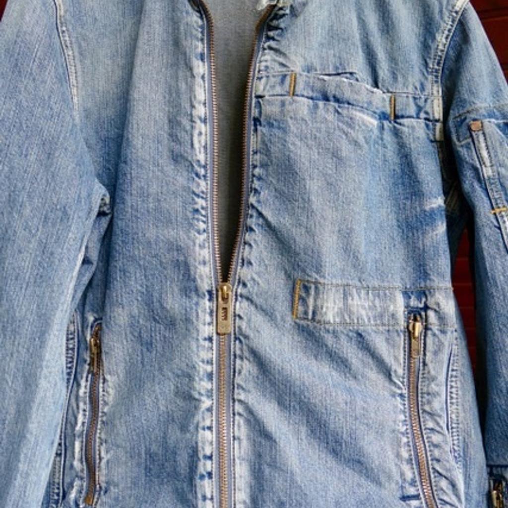 1 sportlich geschnittene Unisex Jeansjacke von G-Star in der Gr. L/52. Die Jacke mit lässigem Stehkragen und Druckknöpfen hat 2 seitliche Taschen mit Reißverschlüssen und 1 aufgesetzte Brusttasche.