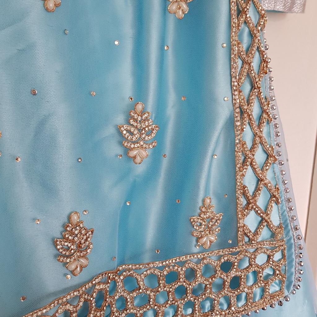 Lovely lengha with heavy diamonte stone work detail on top and gold thread embroidery. Also some pearl work. Discrete zip in back.

Net skirt has diamonte as well. It has 4 layers of material including stiff mesh so it has a fuller round shape. Skirt is elasticated with hooks so can be tightened or loosened as needed.

Comes with net scarf with beading and diamonte belt.

Only worn once for 4 hours.

Blue lengha dress
Top length= 75cm

Skirt length= 91cm

Belt= 100cm

Size 32 Indian which I believe is size 10 UK

Any questions please ask. Welcome to see item before purchase.