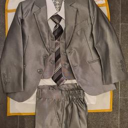 Boys 5 Piece Suit Shiny Grey 2-3 years includes suit cover bag. Near new, only wore once.

Jacket: tailored fit, two inner pockets, two outer flap pockets, 1 handkerchief pocket, single breasted, 2 button fastening, went at the back, fully lined. It boasts a felt fabric 'melton' under the collar that creates a smooth curve and sits properly. Material 25% Cotton, 75% Polyester.

Waistcoat: 3 button fastening, 2 pockets to front, adjustable at the back. Material 25% Cotton, 75% Polyester

Shirt: white shirt with 1 breast pocket. Material 13% Cotton, 87% Polyester.

Trousers: Flat front, zip and 1 button fastening, elasticated waistband at the back, belt loops, 2 side pockets. Material 25% Cotton, 75% Polyester.

Includes a tie.

2-3 Years: Armpit to Armpit 12.5”, Jacket Full Length 16”, Trousers Inseam 15” - measures are estimates.