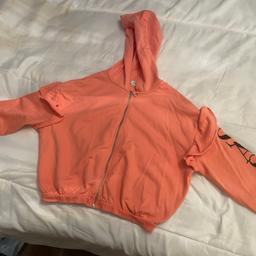 Tangerine coloured girls/ladies zipped hoodie has frill design at top of sleeve and down one sleeve it says in bold black print saying sassy I’m a a size8/10 and it fits okay on me I’d say it was size 10 easily
