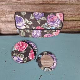 Vintage 1980s purse and matching handbag mirror in pouch. Thin padding. 
Black fabric with pink, purple, and green floral print. Black trim. Zip across back section. Press stud fastening flap over top. 2 inner compartments. 
Round fabric covered mirror attached to case. 
Purse measures 7"×4"
Mirror diameter 3.5"