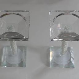 This set of two glass candle holders was never used but is unboxed and stored in the cupboard. They are 15 cm in height. Admire the delicate interplay of light through the glass, accentuated by the charming little beads that adorn the holders' handles. Crafted to accommodate candles of up to 7.5 cm (5 inches) in diameter, these holders are both functional and stylish.