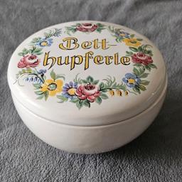 Diese Betthupferle-Keramik-Deckeldose aus den 50er Jahren ist wunderschön. Die weiß glasierte Bonboniere hat eine runde Form und ist handgefertigt. Mit einer Größe von 9,5 x 5,5 x 9,5 cm ist sie klein genug, um auf jedem Tisch oder Regal Platz zu finden. Die Dose hat einen Stempelmarke auf dem Boden, Made in Germany 420.

Die Betthupferle-Dose ist in einem gebrauchten, aber sehr gutem Zustand. Sie ist ein Originalprodukt und nicht antik oder eine lizenzierte Reproduktion. Versand 4,80,- Euro.