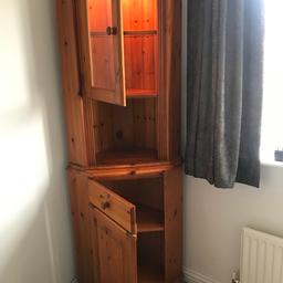 Corner unit in soft pine. Split unit comprising of cupboard space with shelf for the bottom section and a light up top section with glass fronted door with glass shelf. Dimensions are: 190cm height 40cm depth 40cm width