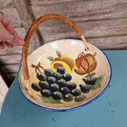 Vintage circa 1960s Puigdemont earthenware stone large fruit bowl. Natural cane collapsible top handle with loops through holes in the sides. Glossy painted raised fruit design. Blue painted underneath. 
Signed base. 
Made in Spain. 
Diameter 10.7"
There's a hairline crack to the enamel on the edge....see pics