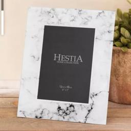 Display your cherished memories in style with this stunning Hestia Home Collection photo frame. The rectangular frame features a beautiful white marble effect with marbled pattern that will complement any home decor.

Measuring 13cm x 18cm (this is the photo area, not the actual frame dimensions) this portrait-oriented photo frame is perfect for holding a 5” x 7" photograph. Crafted from high-quality glass material, this photo frame not only adds elegance to your living space but also provides longevity. Ideal for any room in your home, this Hestia Home Collection photo frame is a perfect addition to your photo display collection.

Please note: this frame is free standing only and is NOT suitable for hanging on the wall.