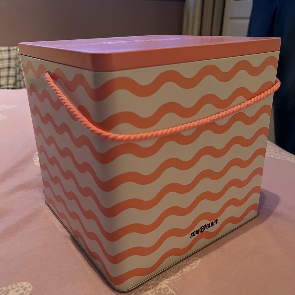 Peach/pink empty Soap & Glory gift tin, with rope handle, which can be filled and used for gifting. Can hold at least half a dozen full size toiletry items. Or can be used to store other toiletries or cosmetics.