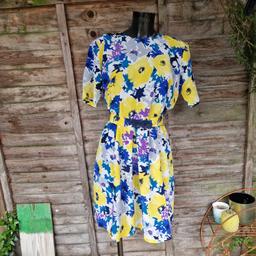 Vintage 1980's handmade dress. Bright blue, white, and yellow floral print. Short length flippy skirt. Elasticated waistband. Matching belt with navy blue plastic floral clasp fastening. Short sleeves. 3d flower shaped button up back. No labels. 
Chest measures 40"
Waist measures 30"-34"
Length 38.5"
Approximate size 10-12