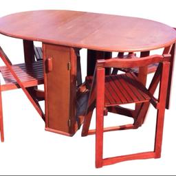 An oak veneered folding dining table and chair set with two leaves supported on gatelegs flanking doors enclosing four A-frame folding chairs. (53.75 in x 33.75in x 29.5in)