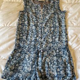 This beautiful blue floral playsuit is perfect for the summer. It has a drawstring waist cord with a metal seashell trim at the end. There are 2 flattering pockets, the left side pocket has a decorative metal button. You will also find decorative stitching around the neckline and on the frills around each armhole.